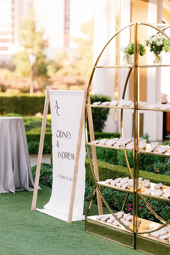 Wedding seating chart on a wooden easel with calligraphy linen banner and green hydrangea bud vases in a manicured garden setting