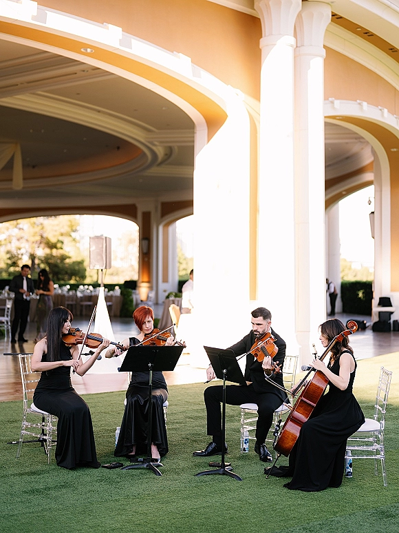 Wedding ceremony musicians in black performing as a string quartet wedding with violins and cello under a golden-hour pavilion with arches