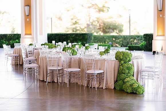 Reception tablescape with round wedding reception tables in champagne linens, clear acrylic chairs, and green hydrangea centerpieces on a covered patio