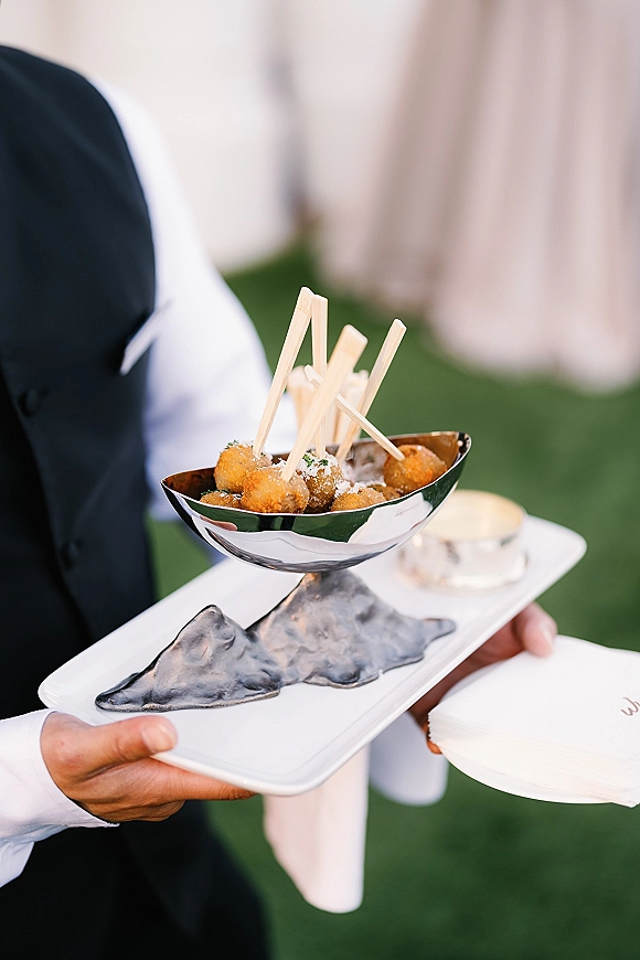 Wedding cocktail appetizers on a passed hors doeuvres tray with fried bite-size bites, wooden picks and napkins, served outdoors on a lawn