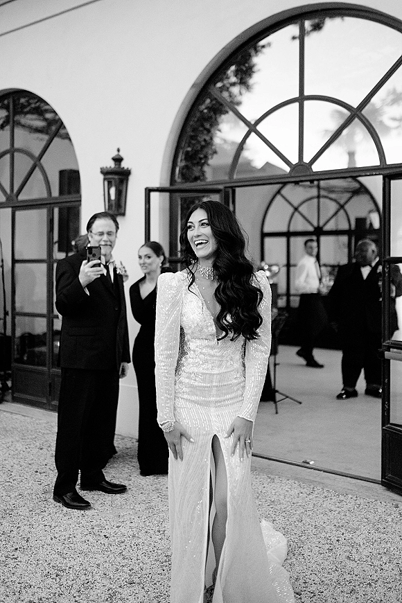 Bride portrait in a long sleeve wedding dress, laughing in a beaded deep V gown with choker by arched glass doors in a courtyard