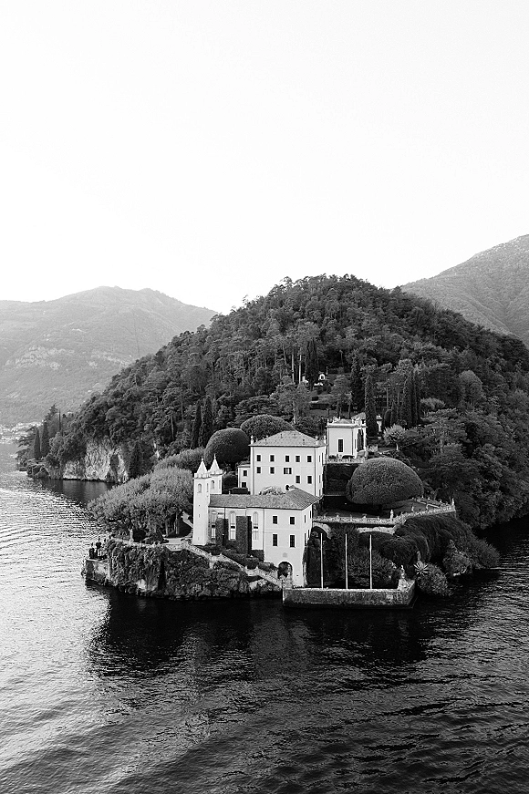 Wedding venue exterior overlooking a lakeside wedding venue, with stone villa terraces, hedges, and trees set against mountains and shoreline