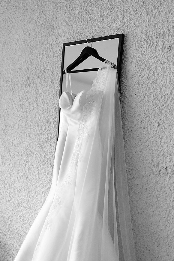 Wedding dress in a framed mirror, strapless satin wedding dress on a hanger with lace-trim veil draped against a textured wall