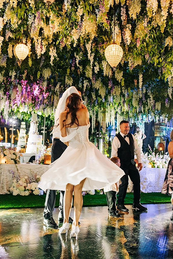 First dance as bride twirls in wedding first dance, veil and corset-back gown flowing under hanging florals and lantern lights at night