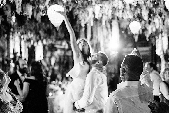 Wedding reception dance as bride and groom sway on a crowded dance floor under hanging greenery and lantern lighting in a dim venue