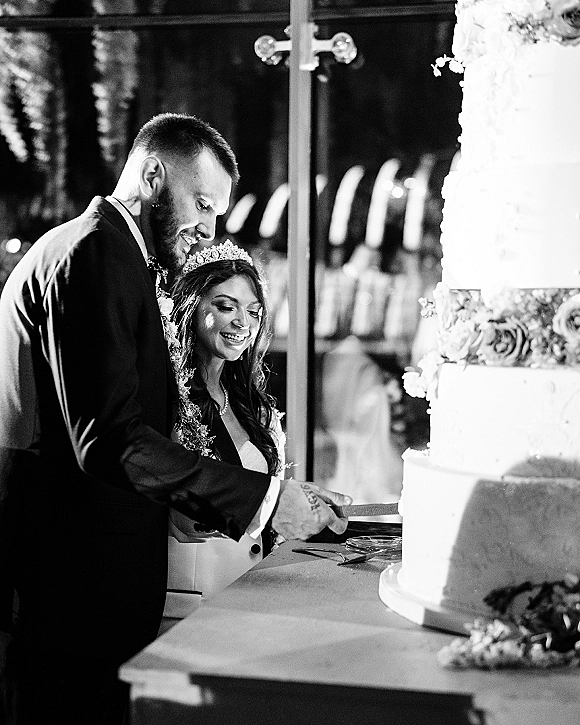 Cake cutting by bride and groom cake cutting a tall white tiered wedding cake with knife and server at a reception table with guests