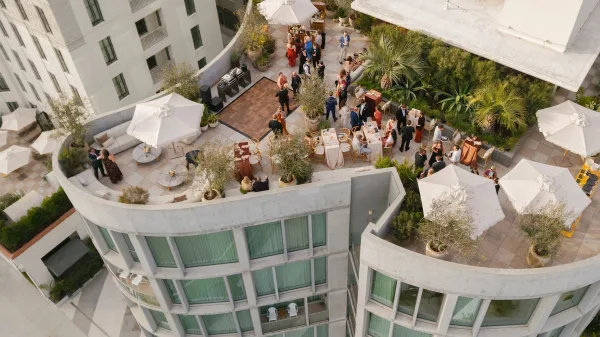 Rooftop wedding reception with round tables in white linen, patio umbrellas, lounge seating, and a small dance floor on a modern terrace