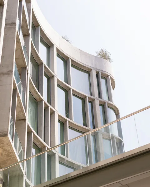 Modern venue exterior with a curved concrete facade and large glass windows, topped with rooftop greenery against the sky