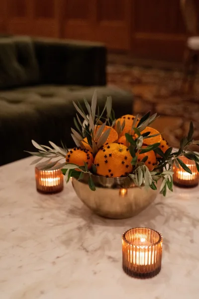Wedding centerpiece styled as a citrus centerpiece, featuring oranges clustered on a marble tabletop with a velvet sofa in the background.