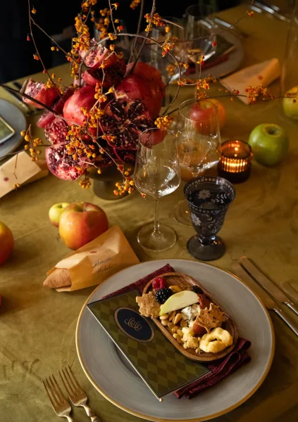 Reception tablescape for an autumn wedding table with a lush fruit centerpiece on an olive tablecloth, softly lit by candlelight.