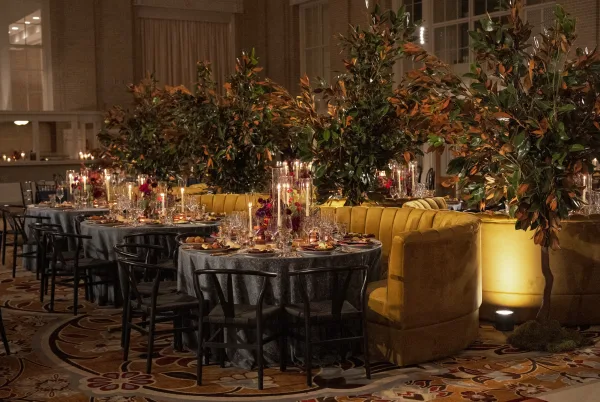 Reception tablescape aglow for a candlelit wedding dinner, framed by a velvet banquette against ballroom drapery and tall windows.