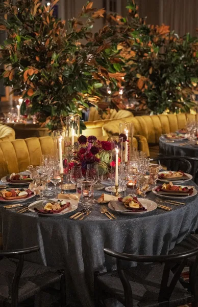 Reception tablescape styled as a candlelit wedding table with gold flatware, set before a velvet banquette and airy greenery branches.