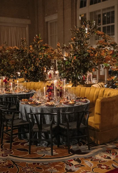 Reception tablescape showcasing indoor reception decor with taper candles, framed by arched windows and soft drapery against a brick wall.