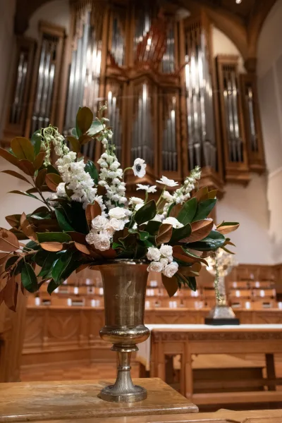 Altar flowers in a brass urn, graceful church ceremony flowers set before a grand pipe organ and wooden choir stalls at the altar.