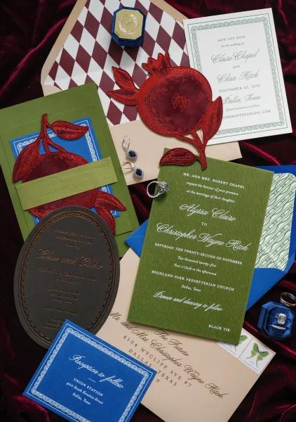 Wedding invitation suite with pomegranate wedding invitations and a die-cut pomegranate accent, styled flat on soft velvet fabric.