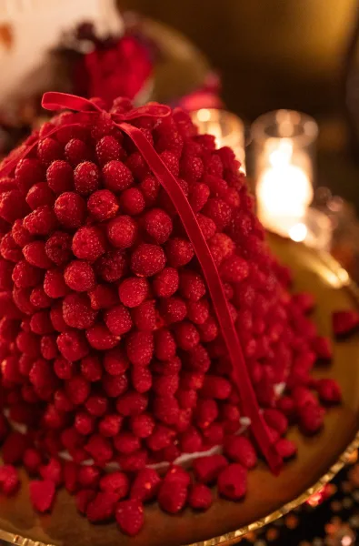 Wedding cake alternative, a raspberry wedding dessert tower wrapped with a red ribbon against a candlelit dark backdrop.