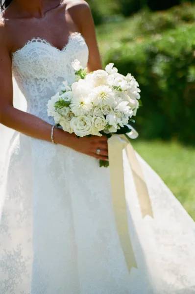 Bridal bouquet, a white bridal bouquet with soft greenery, held by the bride with a trailing ribbon, set amid garden greenery.