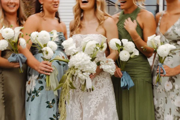 Bridesmaid group photo of bride with bridesmaids in mix-and-match blue and green dresses holding white calla lily bouquets by a white wall