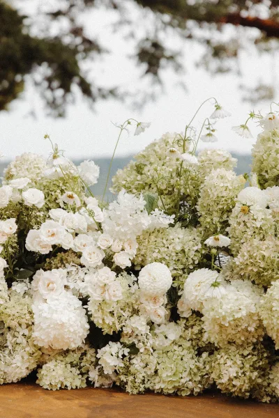 Wedding floral arrangement of white wedding flowers with roses, hydrangeas, dahlias and greenery on the ground, set against outdoor trees and sky