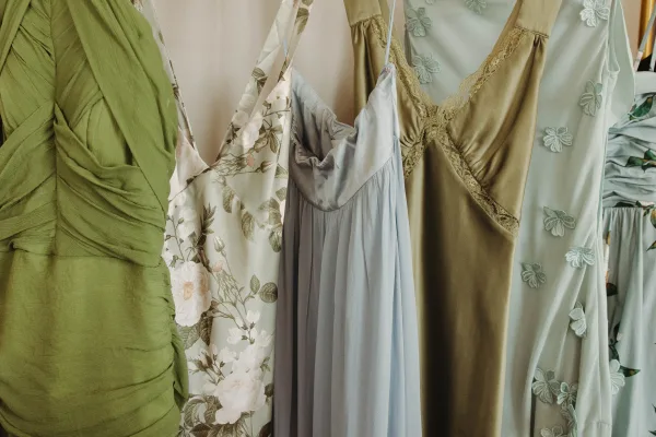 Bridesmaid dresses in a mix and match bridesmaid dresses palette, including floral print and lace trim slip styles, hanging on hangers against a neutral wall