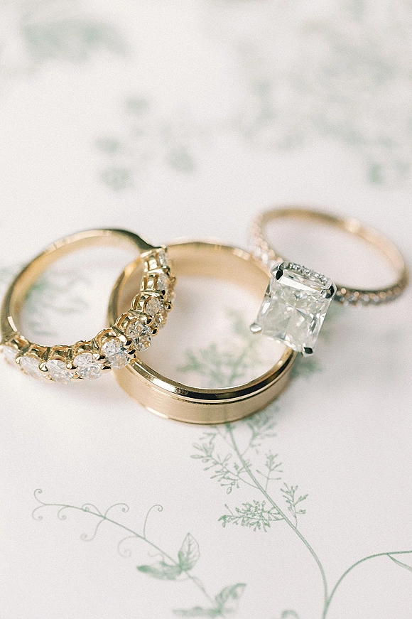 Wedding rings in a wedding ring flatlay, featuring gold bands and diamond eternity and solitaire rings on floral patterned paper