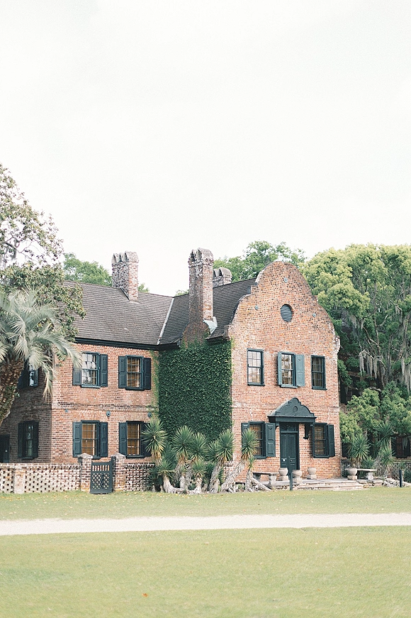 Wedding venue exterior of a historic brick wedding venue with ivy and black shutters, potted planters by the front door, lawns and palms beyond