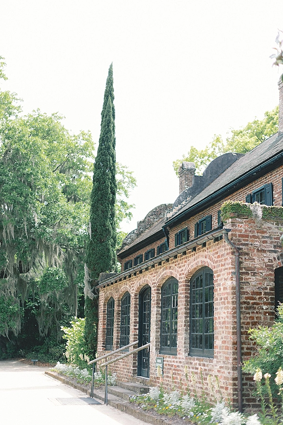 Wedding venue exterior of a brick wedding venue with arched windows, black shutters, ivy, and stone steps along a tree-lined walkway