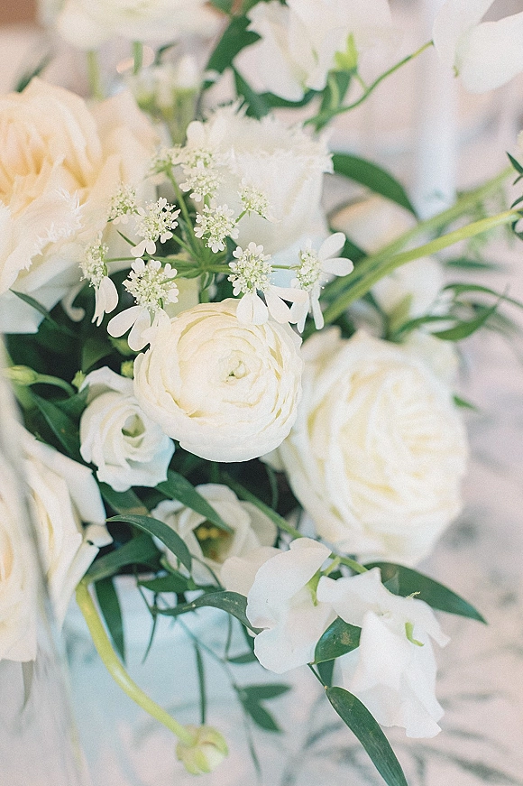 White bridal bouquet of ranunculus with soft greenery accents against a neutral background, showcasing delicate all-white wedding flowers