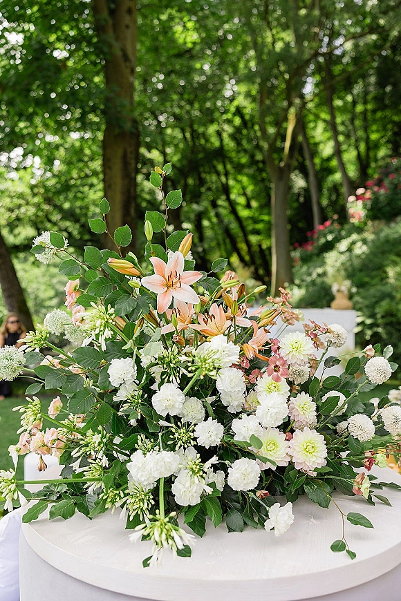 Wedding centerpiece with lush floral centerpiece of lilies, dahlias, white blooms and greenery on a round table in an outdoor garden setting