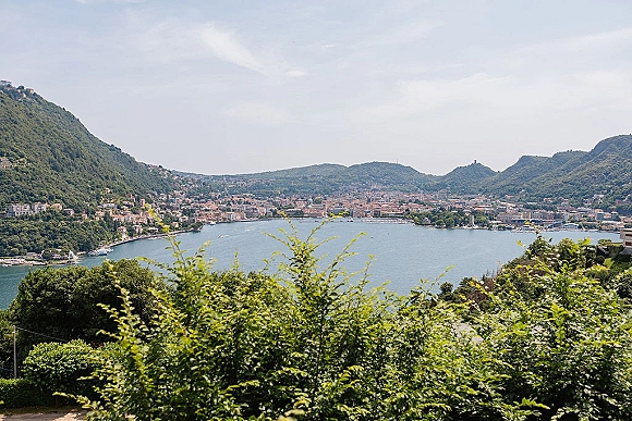 Lake town view with mountain lake panorama, hillside buildings along the shoreline and greenery framing blue water under open sky