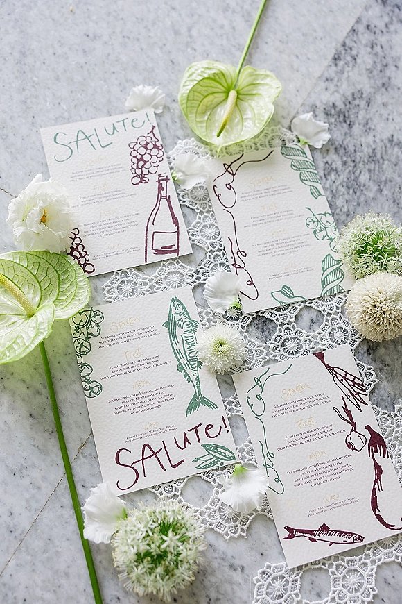 Wedding menu cards with illustrated wedding reception menu details on textured paper, styled with lace runner and anthurium flowers on marble surface