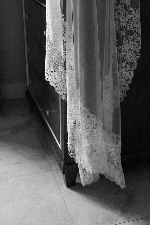 Wedding veil with lace wedding veil trim draped over a dresser, sheer tulle pooling on a tile floor in soft natural light
