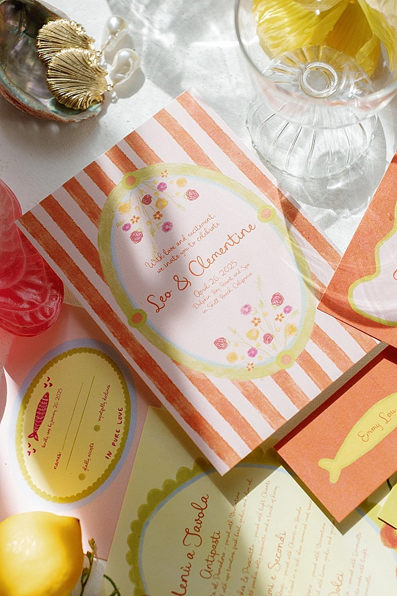 Wedding invitation suite with watercolor wedding invitations, striped card and floral liner, wax seal, lemon, cocktail glass on sunlit tabletop