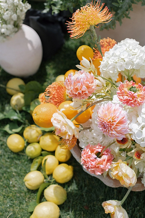 Wedding floral arrangement citrus wedding centerpiece with dahlias, hydrangea, and oranges in a stone bowl on a grass lawn with a white balloon