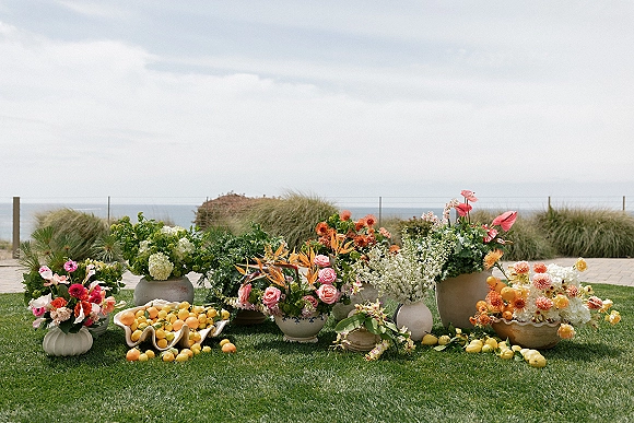 Wedding floral arrangement with ceremony ground florals in ceramic vases, roses and bird of paradise, with lemons on a coastal lawn by dunes
