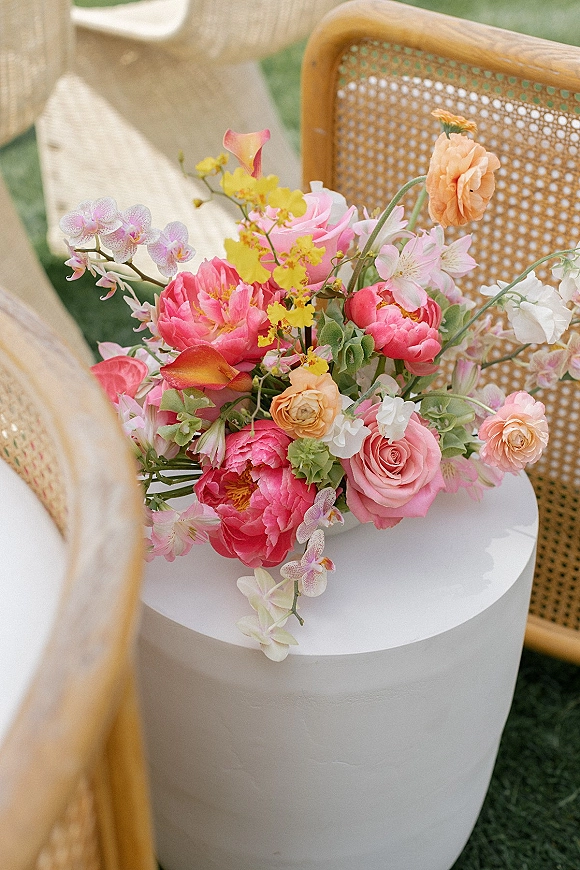 Wedding floral arrangement with ceremony aisle flowers in peonies, roses, calla lilies, and orchids on a white pedestal in sunlight