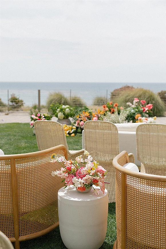 Wedding lounge seating with cane chairs and a white sofa around a side table, accented by a rose centerpiece overlooking the ocean view