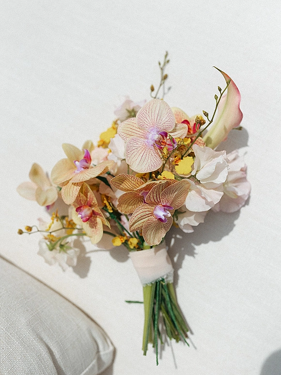 Bridal bouquet with orchid wedding bouquet blooms, calla lilies, yellow fillers and greenery stems, wrapped in floral tape on a white cushion