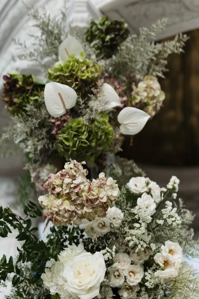 Wedding floral arrangement with white anthurium and green hydrangea in a compote vase, set before a glass greenhouse backdrop