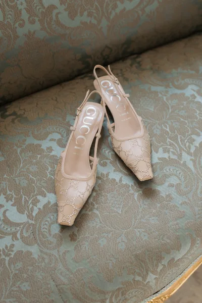 Bridal shoes with beaded bridal heels in slingback, pointed-toe style resting on a patterned damask upholstered chair