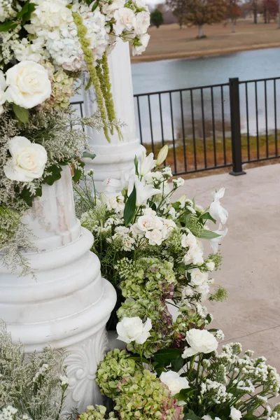 Ceremony floral decor with wedding ceremony flowers of white roses and hydrangeas on columns, set on a lakefront stone patio backdrop