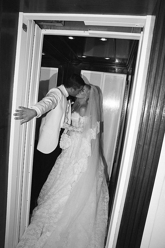 Wedding kiss portrait of bride and groom kissing in a wood-paneled elevator, her long veil and bouquet against his white dinner jacket