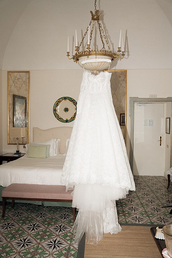 Wedding dress with lace wedding dress details hanging from a chandelier, strapless bodice and tulle skirt in a hotel room