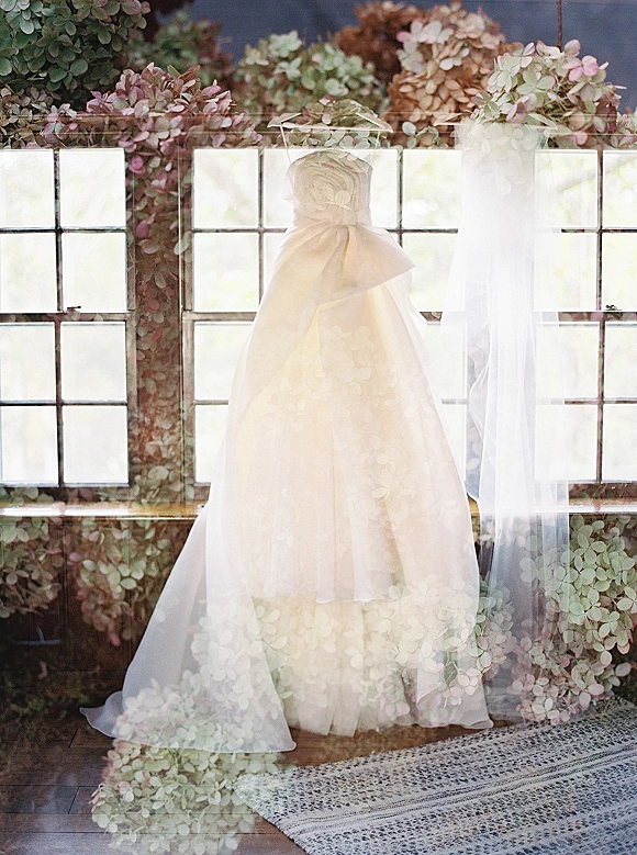 Wedding dress hanging by paned windows, strapless bridal gown with a long veil on the hanger above potted hydrangeas