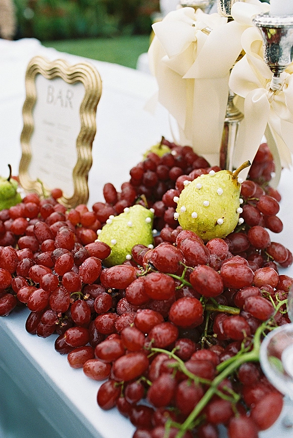Wedding bar decor with a wedding bar sign in a gold frame, silver goblets, grapes and pears arranged on a white tablecloth outdoors
