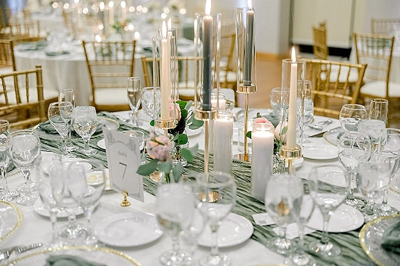 Reception tablescape with wedding table centerpieces featuring taper and pillar candles, blush florals, eucalyptus, gold chargers, and string lights in a ballroom