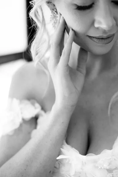 Bridal portrait of a bride touching her face with a soft smile, highlighting a floral applique neckline on her gown