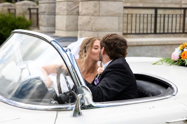 Getaway car kiss between bride and groom in a vintage convertible, a just married car photo capturing their send‑off joy and tender embrace.