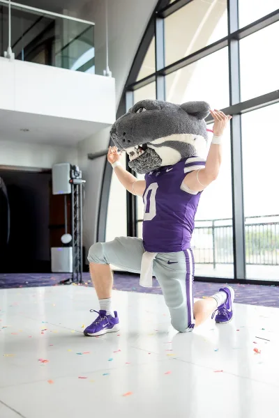 Wedding reception entertainment with a sports mascot at a wedding, confetti swirling in an indoor venue with large windows and a balcony railing