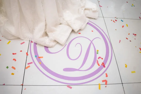 Monogram dance floor with a custom dance floor decal centered on white floor tiles, sprinkled with confetti